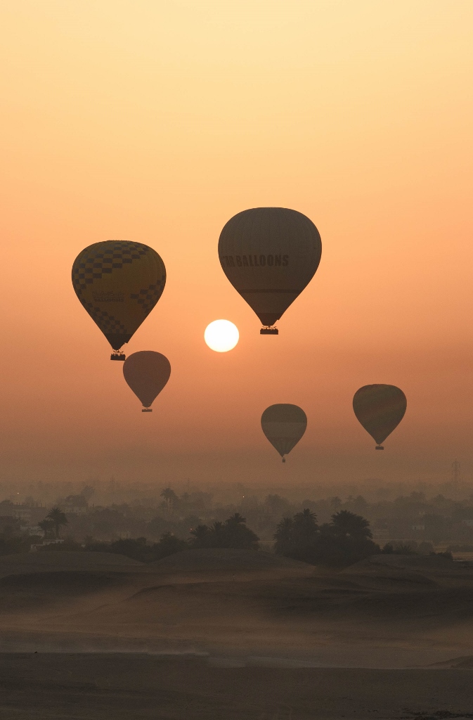 Panorama sur cinq montgolfières au lever du soleil à Louxor