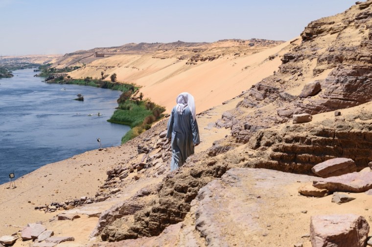 Homme de dos marchant sur les montagnes de dunes face à Assouan